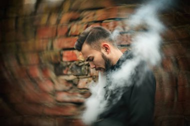 Vape adam. Siyah elbiseli vaping ve elektronik sigara buhar kapalı icar modern saç kesimi ile yakışıklı genç bir beyaz adam fotoğrafı