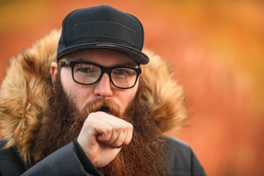 Vape adam gerçek hayatta sakallı. Gözlük ve siyah kap vaping sonbaharında elektronik sigara büyük sakallı genç adam portresi.