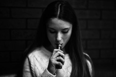 Buharlı genç. İçeride elektronik sigara içen, beyaz tenli, beyaz, genç bir kız. Hayati tehlikesi olan kötü alışkanlık. Vestiyer aktivitesi. Siyah ve beyaz. Siyah ve beyaz