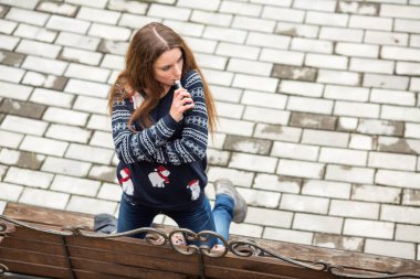 Buharlı genç. Gündelik giysiler içinde genç, beyaz bir kız sonbaharda parktaki bankta elektronik sigara içiyor. Kötü alışkanlık. Vestiyer aktivitesi. Yukarıdan görüntüle.