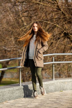 Sonbahar trendi yeşil kıyafet modeli. Genç, beyaz, beyaz, yeşil ceketli, güneşli bir sonbaharda sokakta dolaşan genç bir kız..