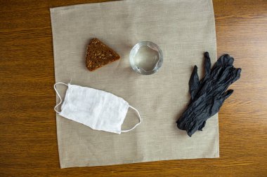 COVID-19. Bir bardak su, siyah eldivenler, beyaz maske ve salgın sırasında mutfaktaki masada bir dilim ekmek. Avrupa 'da Coronavirüs.