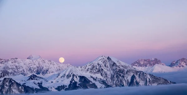 full moon rising over winter landscape and mountains