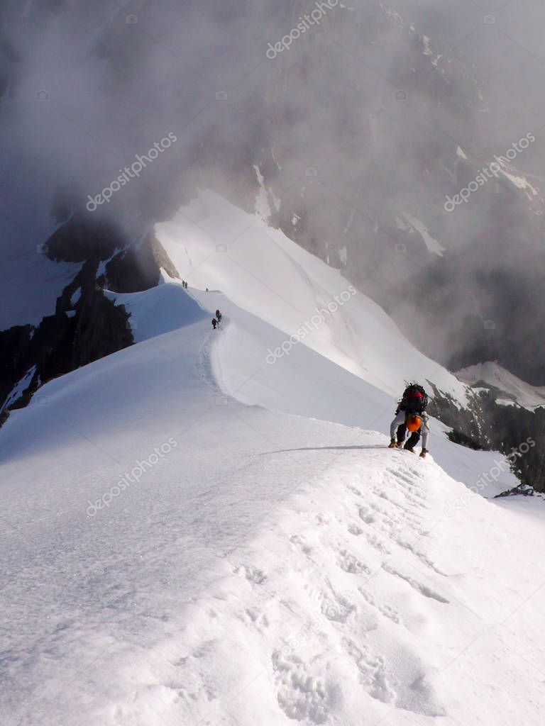 male mountain climber free solo on a narrow and steep summit ridge in the Alps