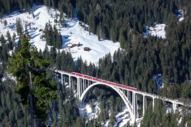 Arosa yakınındaki İsviçre Alpleri'nde kış derin bir geçit üzerinde bir köprü üzerinde kırmızı tren