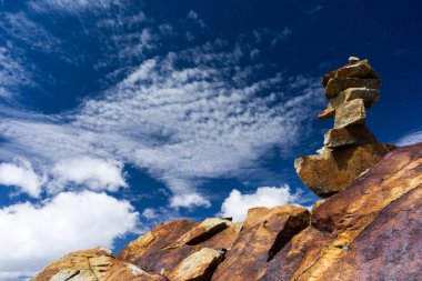 Kırmızı rock cairn beyaz bulutlar ile mavi gökyüzü altında yüksek dağ tepe üzerinde