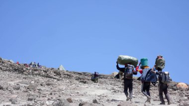 Ağır yükleri ve Kilimanjaro Dağı zirvesine dibinde kamp malzemeleri taşıyan üç erkek hamallar