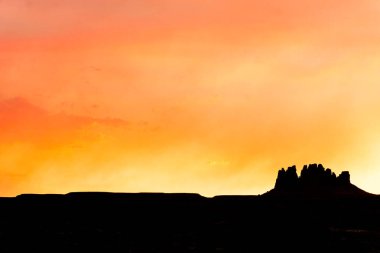 lone mesa rock formation under a fiery red and orange sunset evening sky clipart