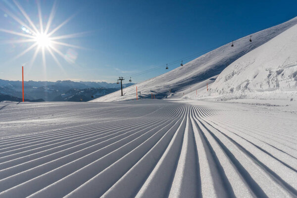 close up view of freshly prepared ski slopes in a ski resort on a beautiful winter day with the sun shining and a great view behind