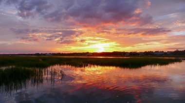 beautiful sunset setting over water and marshlands in the barrier island creekside waters of the South Carolina coast clipart