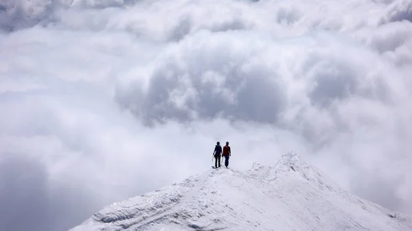 two female mountain climbers on a narrow summit ridge high above cloud banks in the valleys below