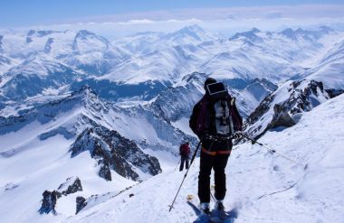 erkek backcountry kayakçı Kayak aşağı üzerinden bir büyük sırt çantası ve güneş paneli ile yüksek bir dağ Zirvesi
