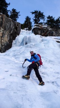 male ice climber in a blue jacket on a gorgeous frozen waterfall climbing in the Alps in deep winter clipart