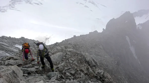 mountain guide and client heading towards a high alpine summit on a foggy day