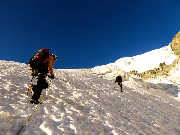 mountain guide and client heading up a glacier towards a high alpine summit on a beautiful summer morning