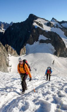 mountain guide and client heading up a glacier towards a high alpine summit on a beautiful summer morning clipart