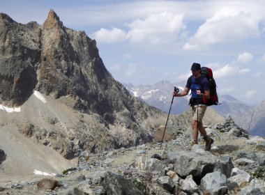 male athletic hiker on his way to a high alpine base camp for mountain climbing walks along a dusty hiking trail in the Barre des Ecrins National Park in the French Alps carrying a large backpack clipart