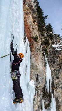 İsviçre Alpleri'nde bir güzel kış gününde dik bir donmuş şelale üzerinde erkek buz dağcı