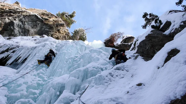 two male ice climbers climbing a frozen ice fall parallel to each other during an ice climbing course