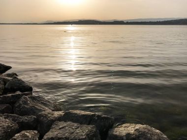ön planda taşlarla Gölü Murten İsviçre'de akşam güneş ve ışık yansımaları ile ve huzurlu göl üzerinde dalgaların