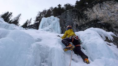 male mountain guide climbing a steep frozen waterfall on a cold winter day in the Alps clipart