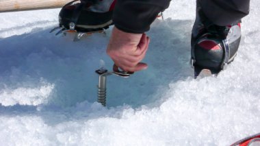 mountain guide screwing an ice screw into glacier ice during a rescue exercise clipart