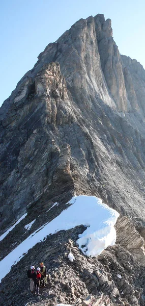 mountain guide leading two male clients to a rocky ridge and onwards to a high alpine summit