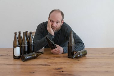 middle-aged alcoholic man with many beer bottles sitting at a wooden table clipart