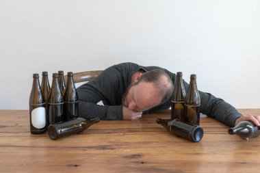 ahşap bir masada oturan birçok bira şişeleri ile orta yaşlı alkollü adam
