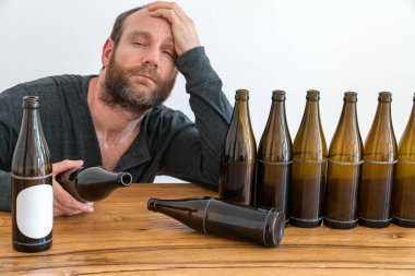 middle-aged alcoholic man with a beard and many empty beer bottles on a table in front of him clipart