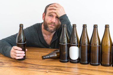 middle-aged alcoholic man with a beard and many empty beer bottles on a table in front of him clipart