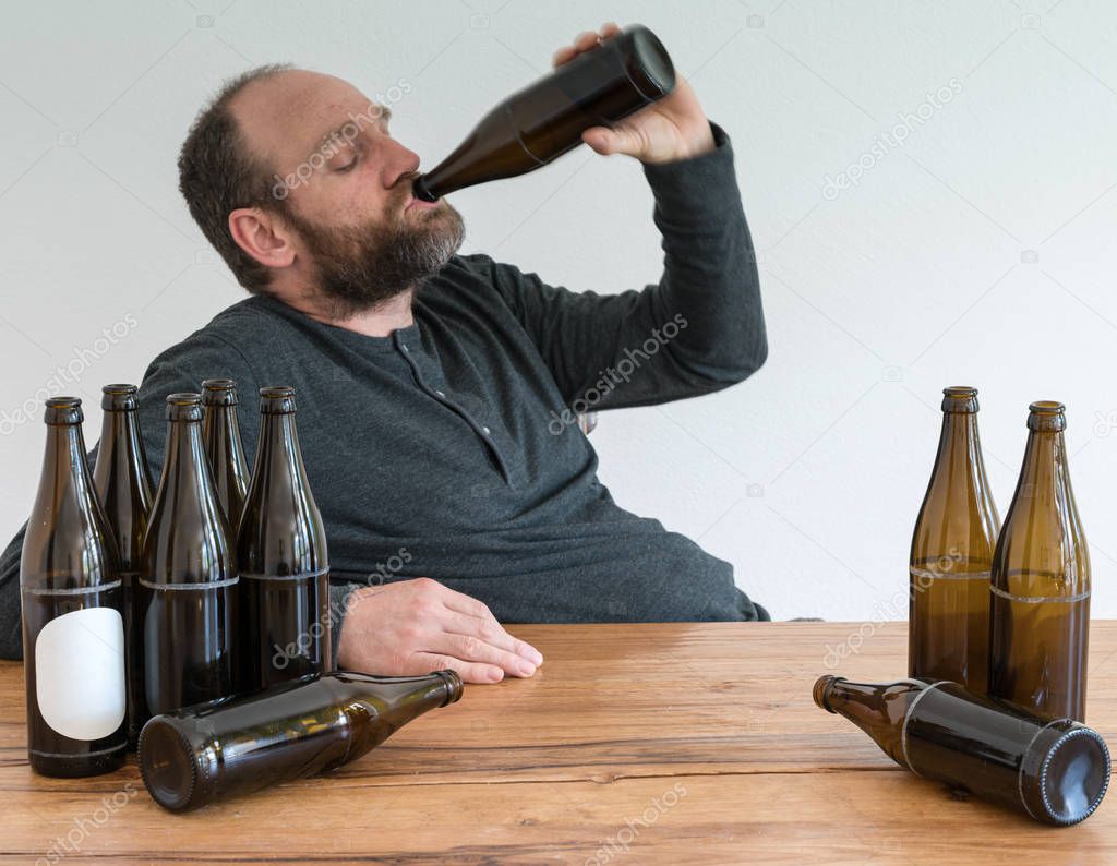 middle-aged alcoholic man with many beer bottles sitting at a wooden table