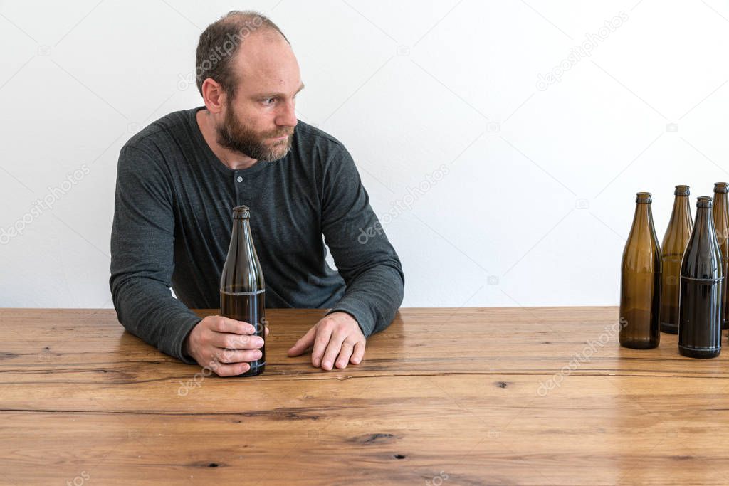 middle-aged alcoholic man with a beard and many empty beer bottles on a table in front of him