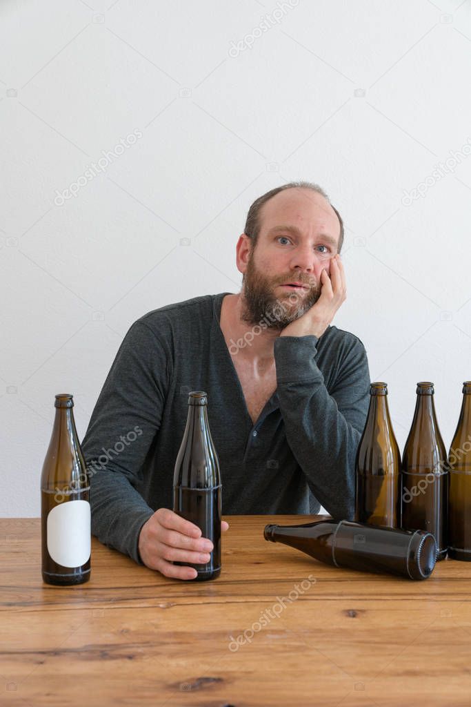 middle-aged alcoholic man with a beard and many empty beer bottles on a table in front of him