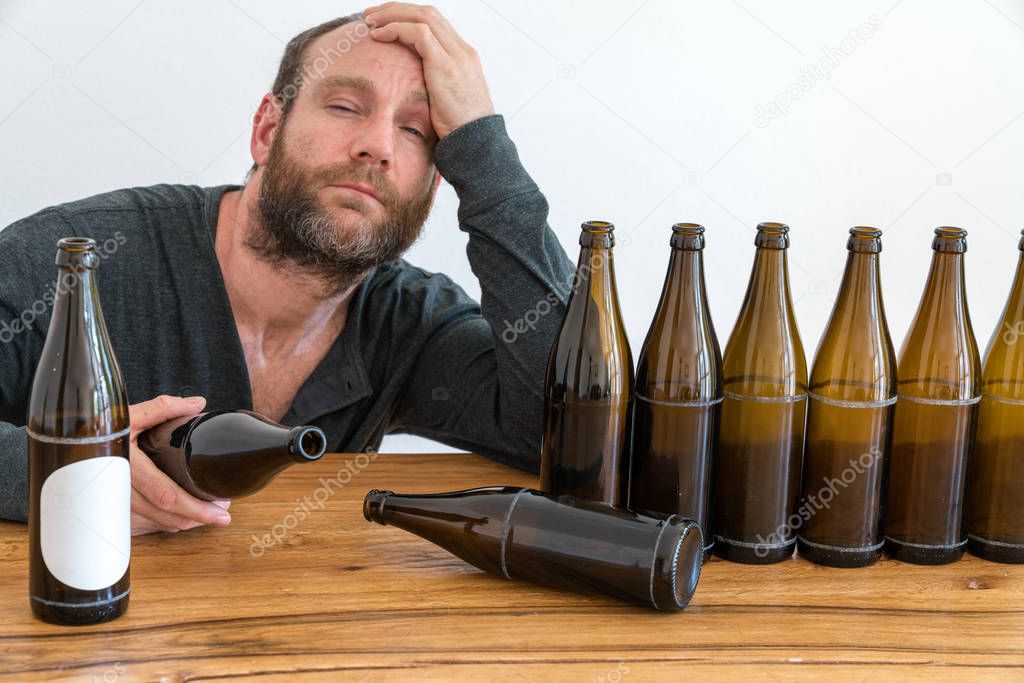 middle-aged alcoholic man with a beard and many empty beer bottles on a table in front of him