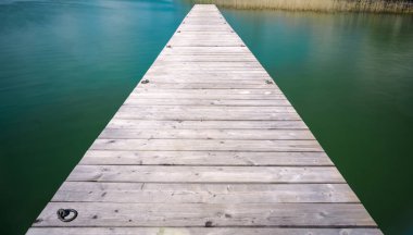 Altın sazlar içinde belgili tanımlık geçmiş bir turkuaz ve Mavi Göl içine uzanan ahşap iskele
