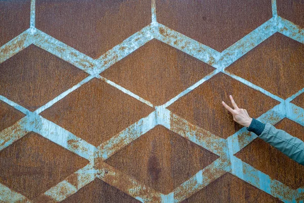 background of rusted vintage metal with a diamond pattern and vintage blue paint and a slender female hand making the peace sign