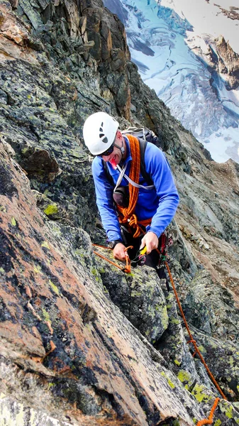male mountain guide building a traditional belay stance with pitons to rappel from a high alpine peak