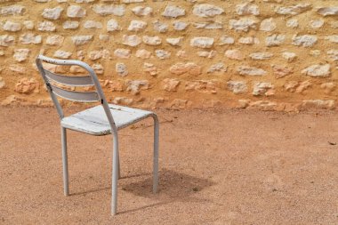 boş beyaz metal sandalye kumlu bir avluda kaya duvarlı