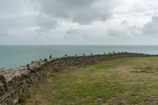 Viejo muro de piedra y vista sobre un océano expansivo bajo un cielo nublado — Foto de Stock