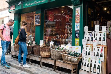 Turistler Honfleur 'daki bir elma şarabı ve içki dükkanında geziniyor ve vitrinlere bakıyor.