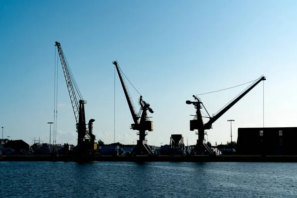 Silueta de grúas portuarias en un gran puerto comercial bajo un cielo azul — Foto de Stock