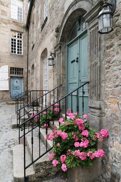 Vista de perto da frente casa de pedra com porta de madeira azul e flores rosa — Fotografia de Stock