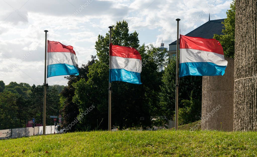 three flags of Luxembourg on a grass field in a strong wind