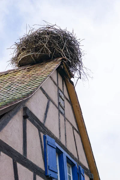 Large stork nest on the roof gable of a traditional wooden half- — Stock Photo, Image