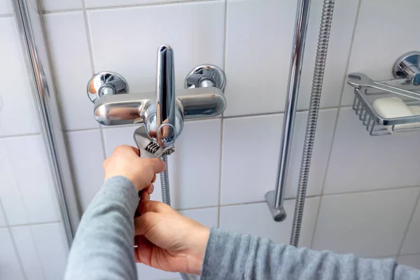 female plumber installing a chrome shower hose on a shower faucet while finishing bath renovation work