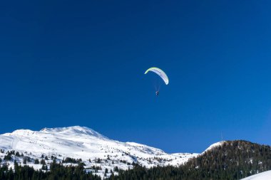 Karlı dağ zirveleri ve mavi gökyüzünde bir paraglider olan bir kış manzarası.