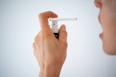 Boğazı ağrıyan ve beyaz arka planda öksüren bir kadın yüzü ve elini sprey ilaçla kapat.