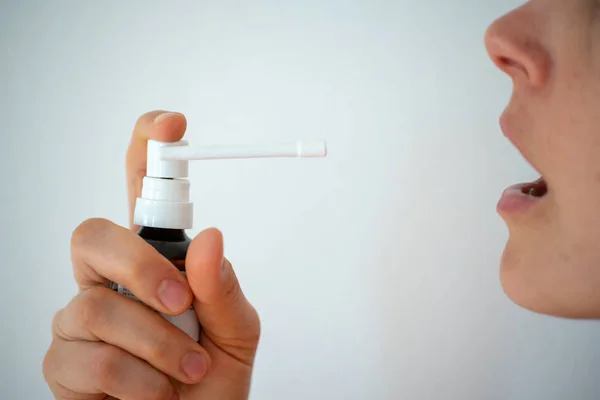 Vista de perto de um rosto feminino e mão com remédio spray para uma dor de garganta e tosse em um fundo branco — Fotografia de Stock