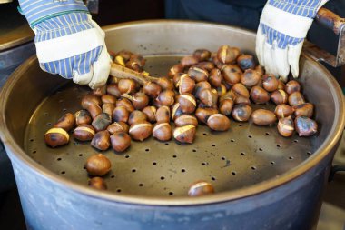 Erkek ellerinin çırpınışını ve lezzetli organik kestaneleri ahşap kepçeyle gaz fıçısında kızartışını görmek.